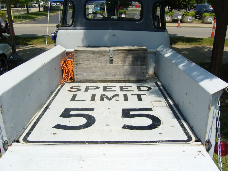 Pickup truck bed interior with a wooden box and orange rope, a "SPEED LIMIT 55" sign is laid flat on the bed floor