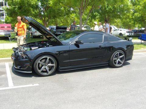 2007 Ford Mustang - A black Ford Mustang is parked with its hood up, displaying the engine bay. Other vehicles and people are visible in the background.