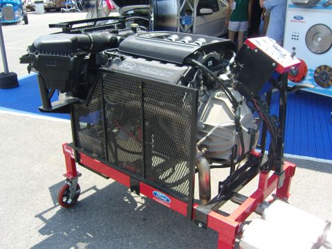 2007 Ford Mustang - A Ford Racing engine is displayed on a red rolling stand with exhaust pipes visible.