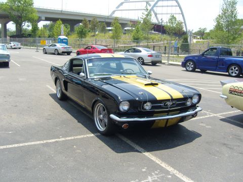 2007 Ford Mustang - A classic black and yellow Mustang is parked in a lot with other vehicles and an overpass in the background.