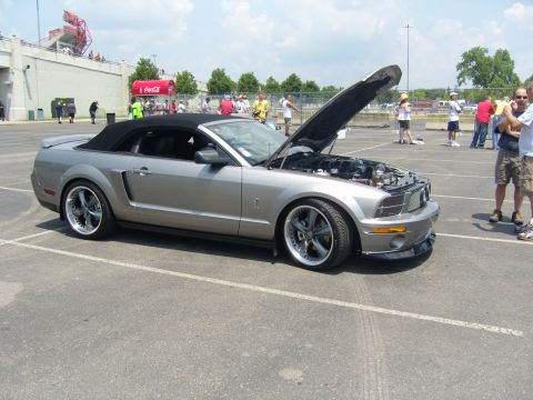 2007 Ford Mustang - A silver convertible Mustang is parked with its hood up, showing the engine bay. People are visible in the background.