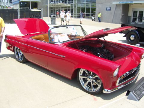 2007 Ford Mustang - A red convertible with its hood and trunk open, revealing the engine and interior, parked outside a stadium.