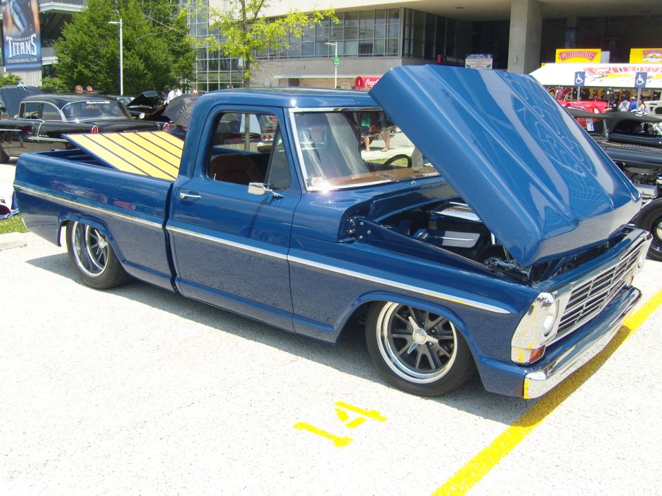 Blue custom pickup truck with wood bed, hood open showing engine. Custom wheels and lowered suspension