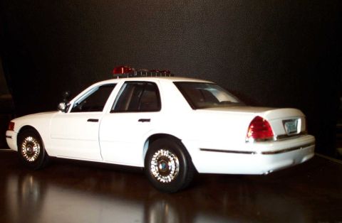 1998 Ford Crown Victoria - A white 1998 Ford Crown Victoria police car is shown from the rear quarter angle with a light bar on its roof.