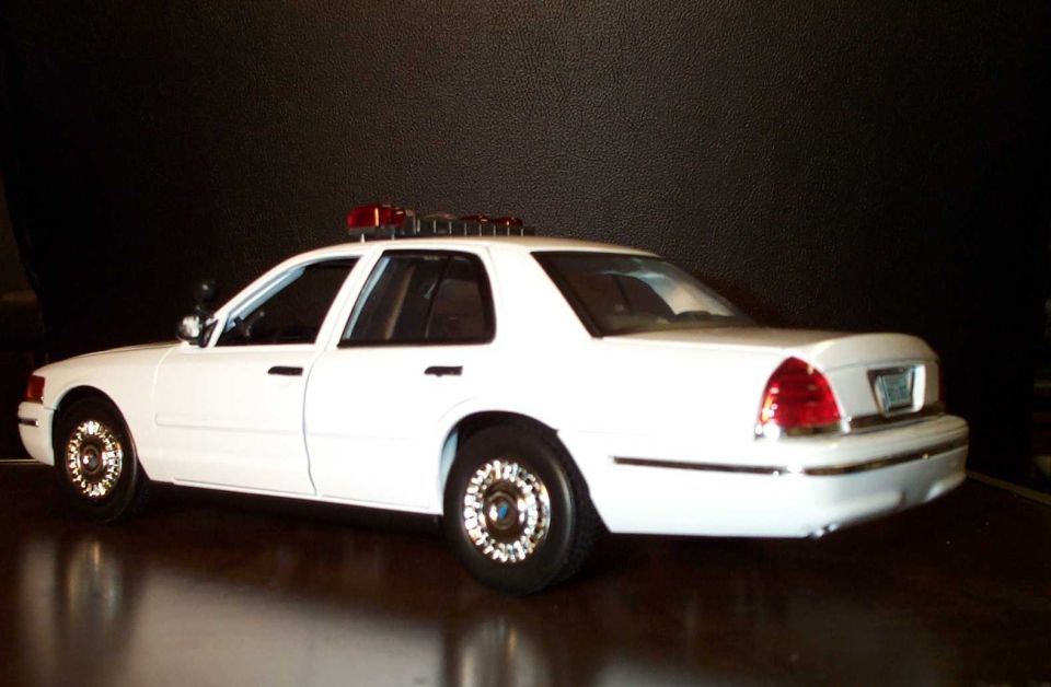 White Crown Victoria sedan with roof light bar, rear side view