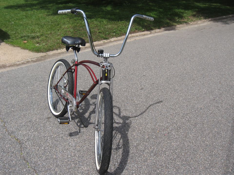 Red cruiser bicycle with tall handlebars and whitewall tires parked on asphalt