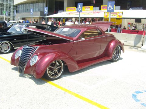2007 Ford Mustang - A custom hot rod coupe is displayed at an outdoor event with vendors and spectators in the background.