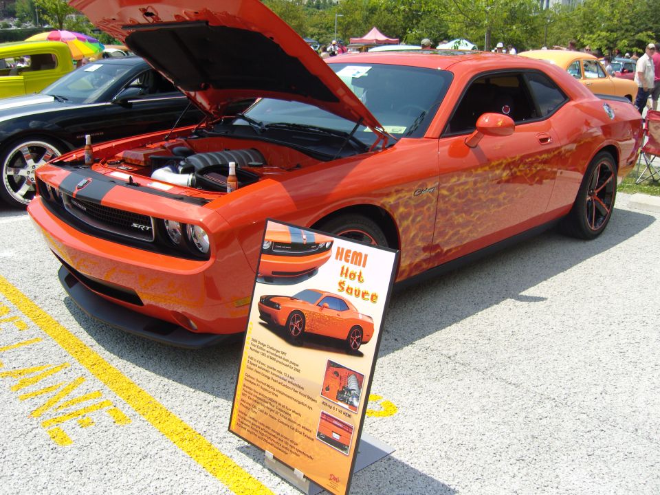 Orange 2011 Dodge Challenger SRT with black racing stripes and flame graphics, hood open, parked at a car show