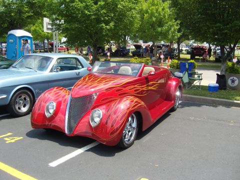 2007 Ford Mustang - A red hot rod with flame graphics is parked next to a blue classic car at a car show.