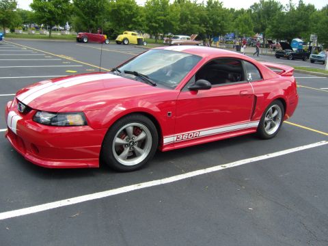 2007 Ford Mustang - Red 2007 Ford Mustang coupe with white racing stripes and "1360R" side decal parked in a lot.