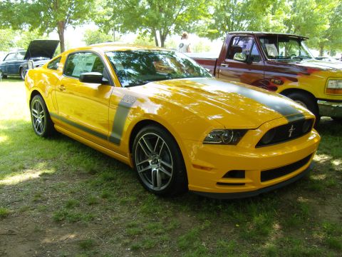 2007 Ford Mustang - A yellow 2012 Ford Mustang Boss 302 is parked on grass next to a pickup truck under trees.