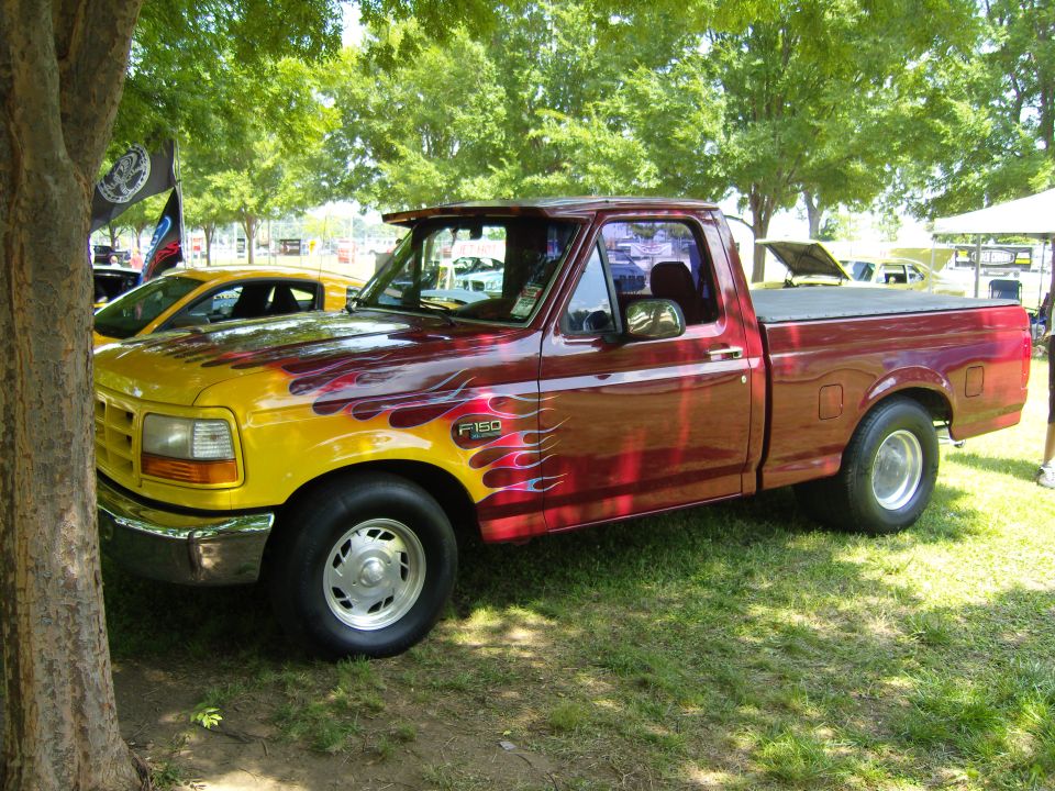 Red and yellow Ford F-150 pickup truck with flame graphics, parked on grass
