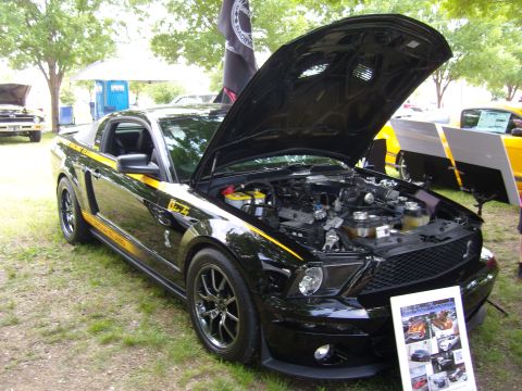 2007 Ford Mustang - A black Ford Mustang with yellow racing stripes is displayed with its hood open at an outdoor event.