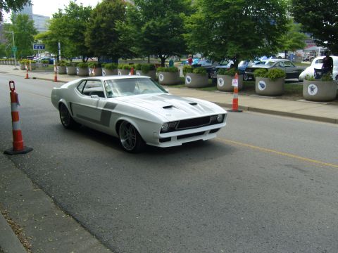 2007 Ford Mustang - A classic white Mustang with racing stripes drives down a city street.