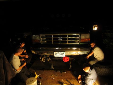 1992 Ford Bronco - Mechanics work on the front suspension of a 1992 Ford Bronco at night.