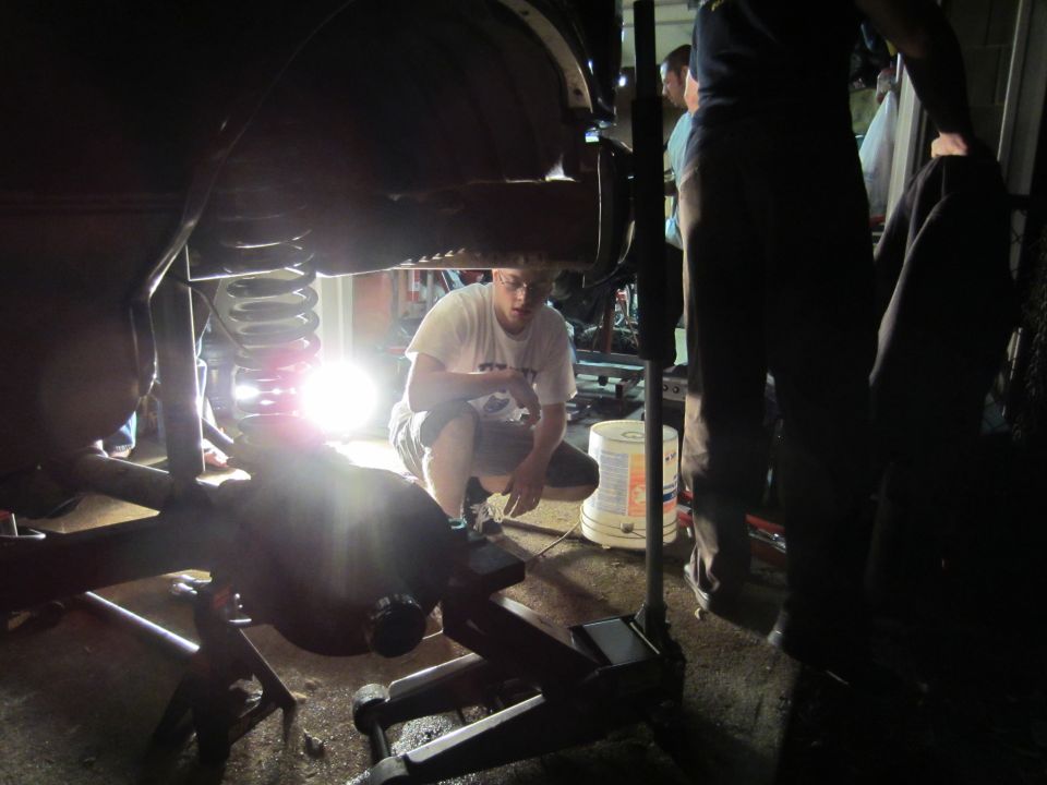 guy working on vehicle suspension, jacked up in garage