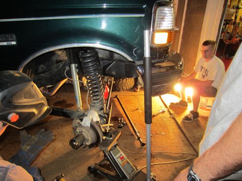 1992 Ford Bronco - Mechanics work on the front suspension of a green 1992 Ford Bronco in a garage.