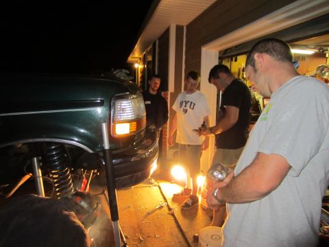 1992 Ford Bronco - A group of men work on the front end of a green 1992 Ford Bronco at night.