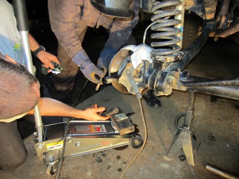 1992 Ford Bronco - Close-up of vehicle suspension work, showing a floor jack and jack stand supporting the vehicle's front end.