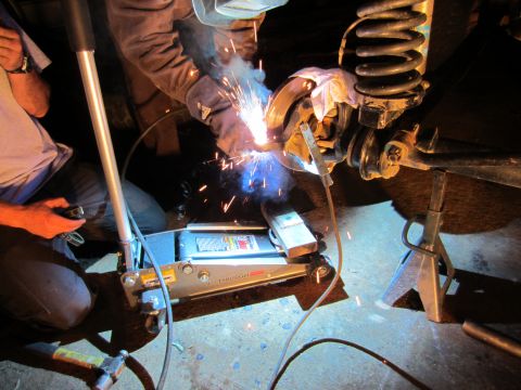 1992 Ford Bronco - Someone is welding a part of a vehicle's suspension system while it's lifted on a jack and jack stand.