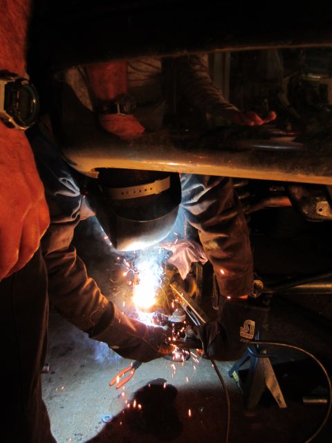 1992 Ford Bronco - Mechanic performs welding repairs on the underside of a vehicle, illuminated by bright sparks.