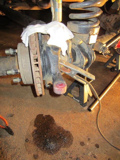 1992 Ford Bronco - A vehicle's suspension component, likely undergoing maintenance, is supported by jack stands on a concrete floor.
