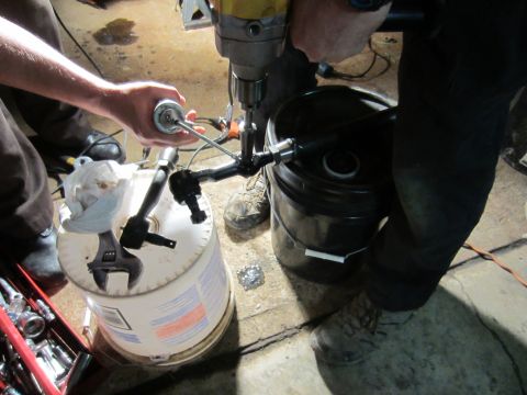1992 Ford Bronco - Plumbing parts are being worked on with a drill, supported by buckets and tools.