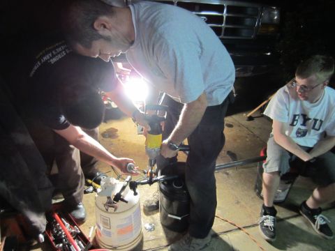 1992 Ford Bronco - Several people are gathered around the front of a truck, appearing to work on a mechanical part.