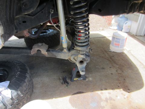 1992 Ford Bronco - Front suspension component being worked on, supported by a jack stand. A tire lies nearby.