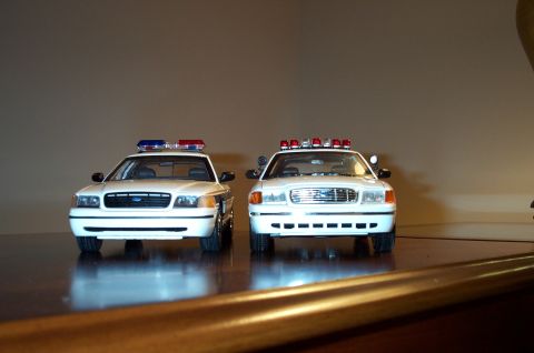 1998 Ford Crown Victoria - Two white police car models, likely 1998 Ford Crown Victorias, are displayed side-by-side from the front.