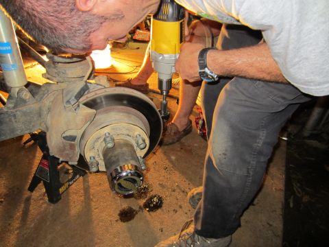 1992 Ford Bronco - Mechanic works on a vehicle's front axle, which is supported by jack stands.