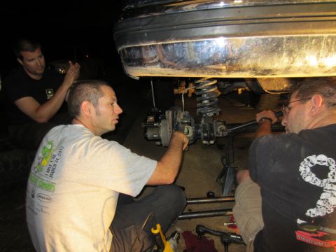 1992 Ford Bronco - Three men are working on the suspension of a vehicle, with the rear bumper and axle visible.