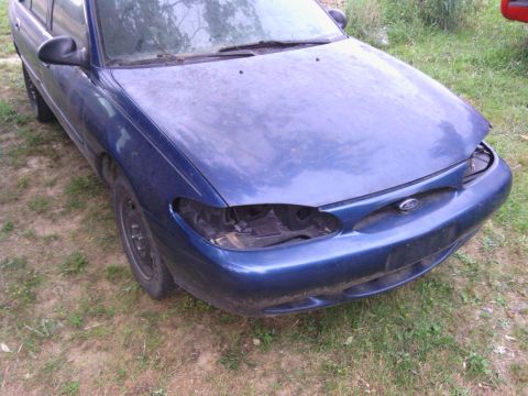 1999 Ford Escort - This blue 1999 Ford Escort sedan is shown from the front, missing both headlights.