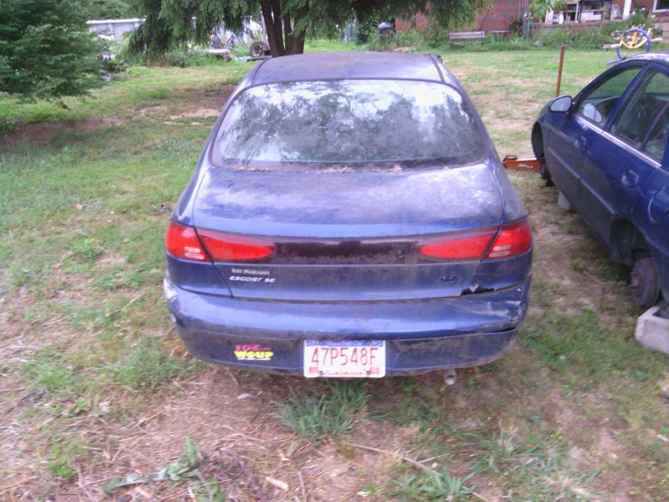1999 Ford Escort SE rear view, blue, with damage to rear bumper and another blue car parked to the right