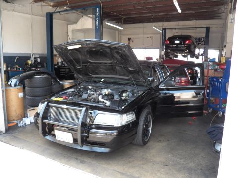 2003 Ford Crown Victoria - Crown Victoria on a shop floor with hood raised, intercooler mounted behind a chrome push bar.