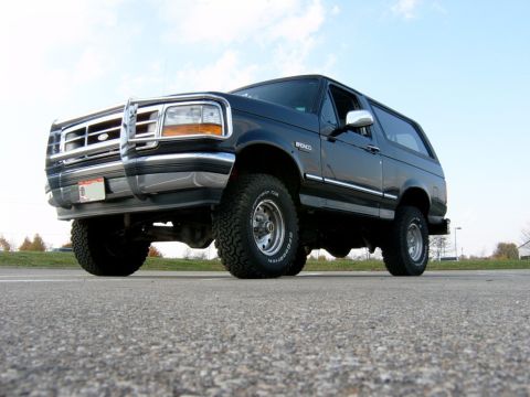 1995 Ford Bronco - This black Ford Bronco is shown from a low angle, highlighting its off-road tires and chrome accents.
