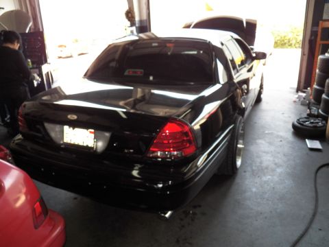 2003 Ford Crown Victoria - Black Crown Victoria parked rear-out in a shop bay, taillight and chrome-lip wheel in view.