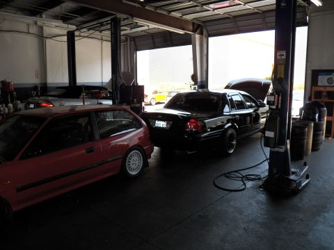 2003 Ford Crown Victoria - Crown Victoria parked next to a red Honda Civic hatchback in a garage with a two-post lift.