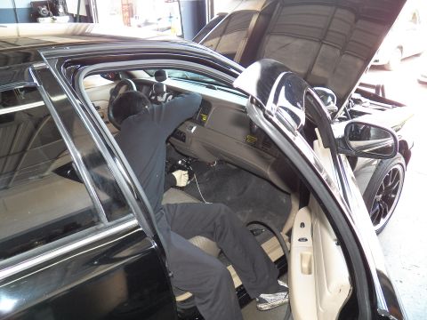 2003 Ford Crown Victoria - Worker leans into the footwell of a black Crown Victoria, hood up, beige interior and door panel visible