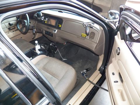2003 Ford Crown Victoria - Driver-side cabin view with beige dashboard, center screen and a water bottle in the console