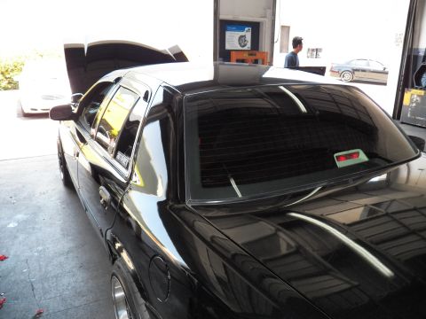 2003 Ford Crown Victoria - Glossy black quarter panel and dark-tinted rear glass of a sedan parked under a shop light