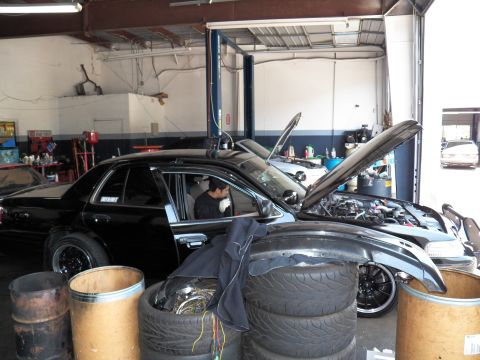 2003 Ford Crown Victoria - Sedan on shop floor, hood raised, performance tires and barrels in foreground