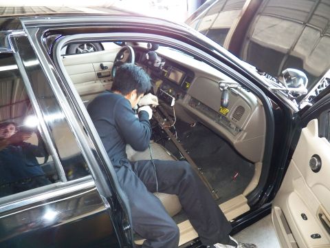 2003 Ford Crown Victoria - Worker servicing the lower dash of a Crown Victoria, exposed sill rail and wiring visible