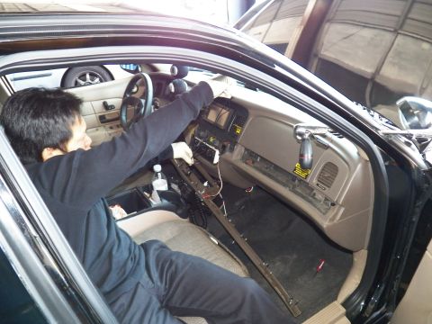 2003 Ford Crown Victoria - Worker services the center dash of a beige-interior sedan with sill trim removed