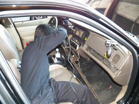 2003 Ford Crown Victoria - Technician services the lower dash of a beige-interior sedan, sill rail removed