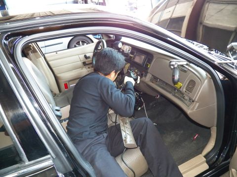 2003 Ford Crown Victoria - Gloved worker reaches into the passenger footwell of a black sedan with tan interior during an equipment install.