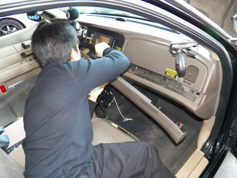 2003 Ford Crown Victoria - Worker fits wiring behind a tan dash with a digital display and yellow airbag warning label.