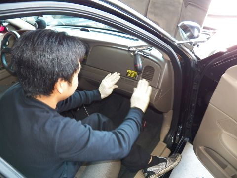 2003 Ford Crown Victoria - Worker presses both gloved hands against the tan dash trim, yellow warning label between them.
