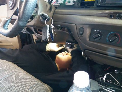 2003 Ford Crown Victoria - Worker on his back routes wiring under the column beside an aftermarket steering wheel.
