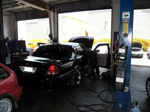 2003 Ford Crown Victoria - Black sedan raised on a lift with hood open as a technician works at the front fender.